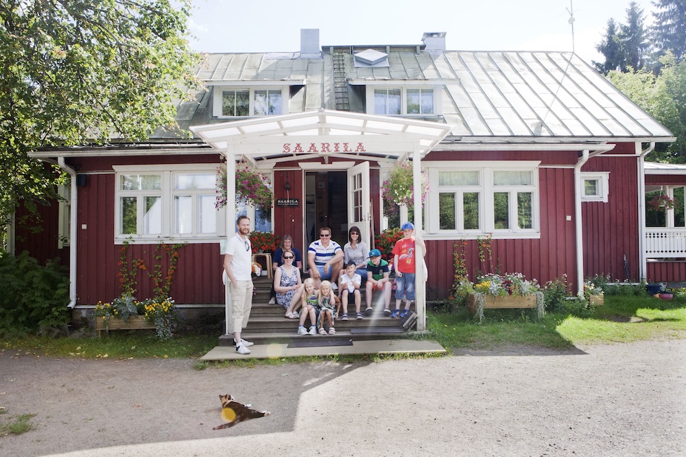Joukko ihmisiä hymyilee tyytyväisesti maatalon pihalla